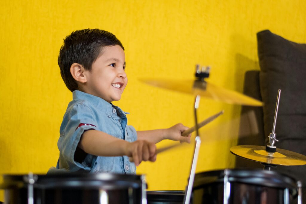 A kid joyfully learning to play drums online, demonstrating the dynamic and engaging musical education provided by MasterMindz