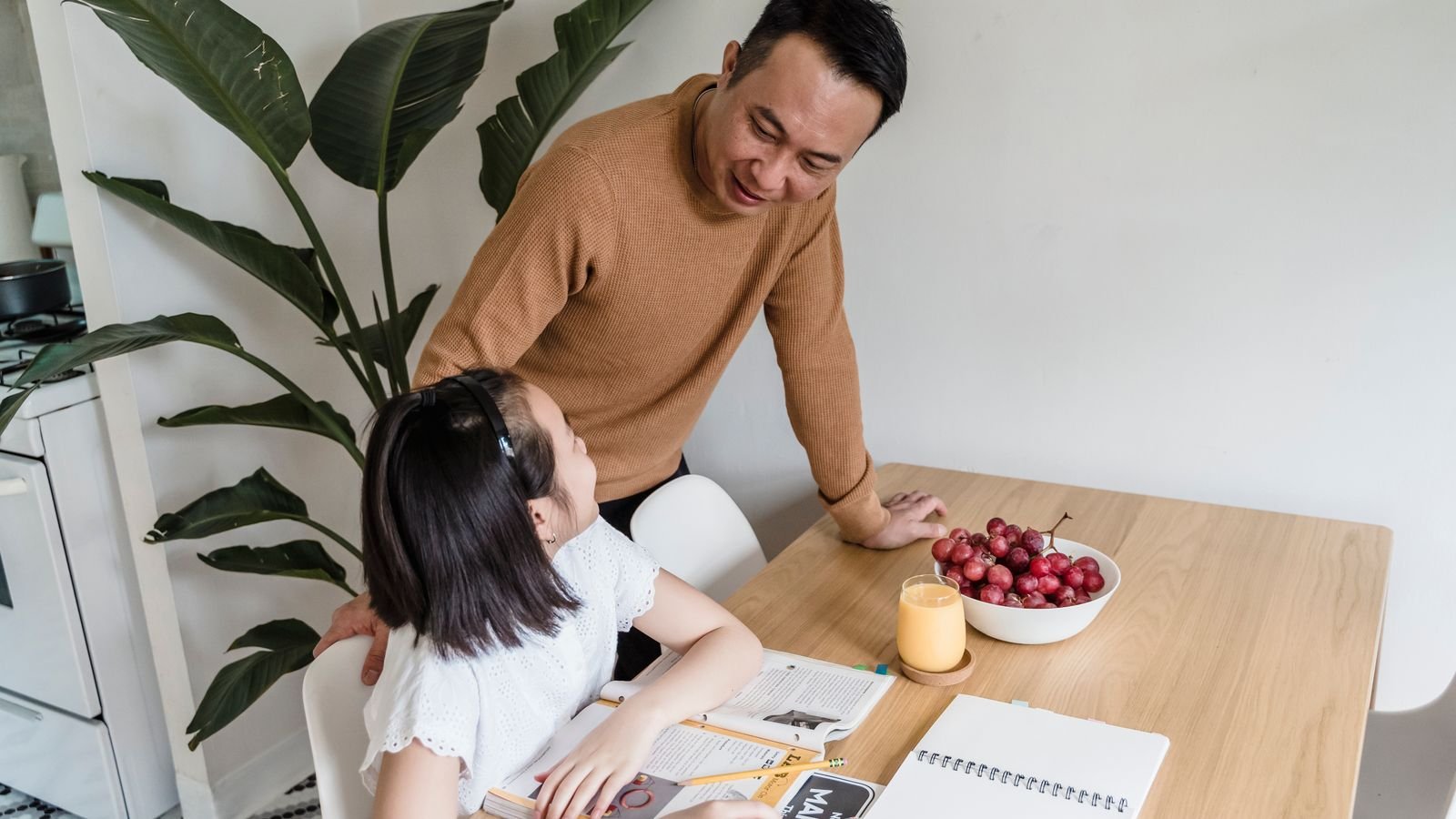 Parent sitting calmly beside a child doing homework at a tidy table, ending nightly homework battles