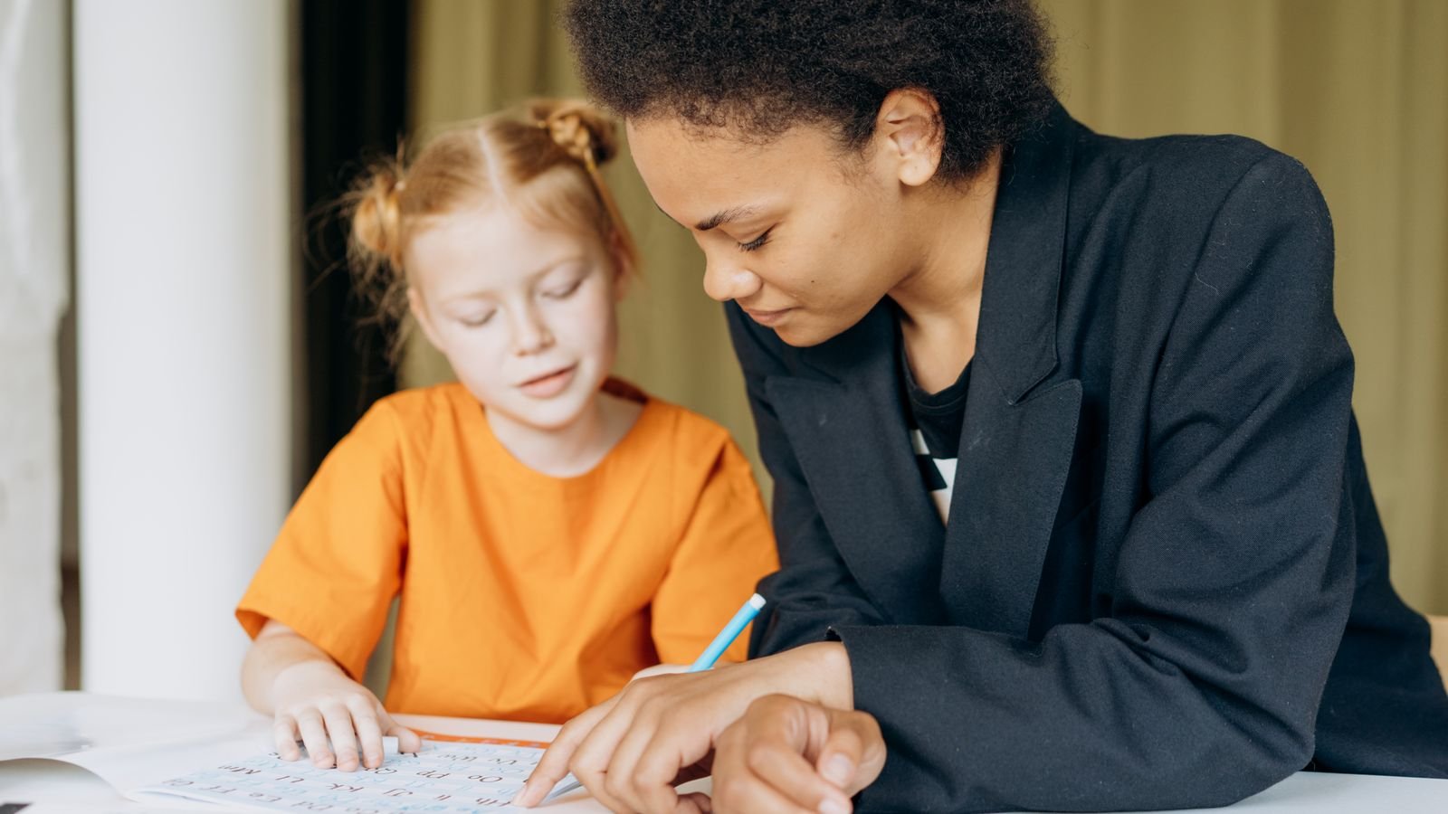 Kindergarten child learning block coding on a tablet with an adult guiding the lesson