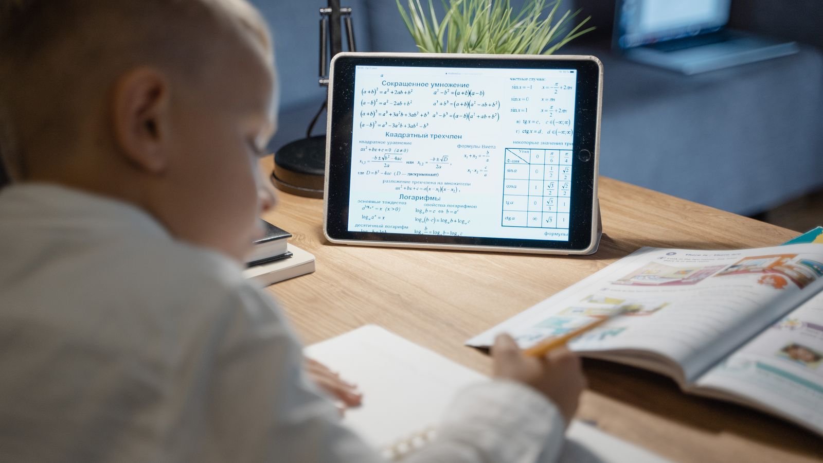 Child doing maths homework beside a chessboard, showing how chess thinking transfers to schoolwork