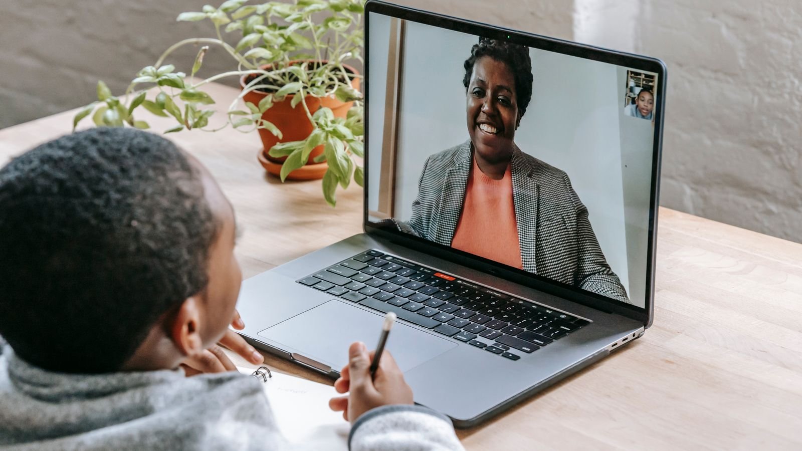 Child taking a live 1 on 1 online tutoring class with a tutor visible on the laptop screen