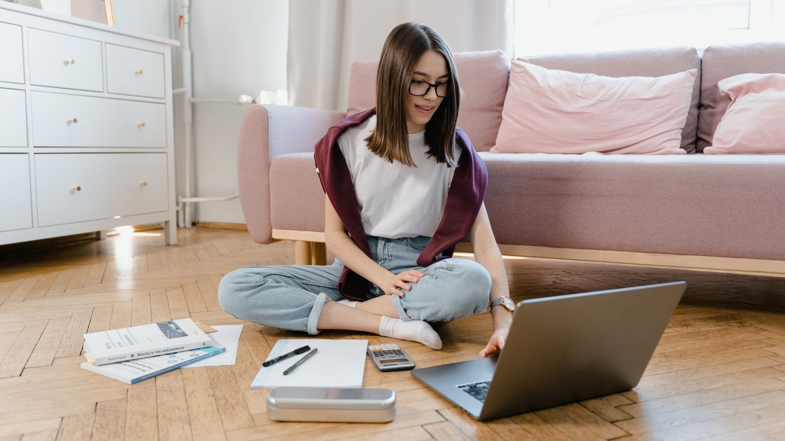 Child taking a live online class on a laptop in a shared family room with a parent nearby, showing safe online class setup