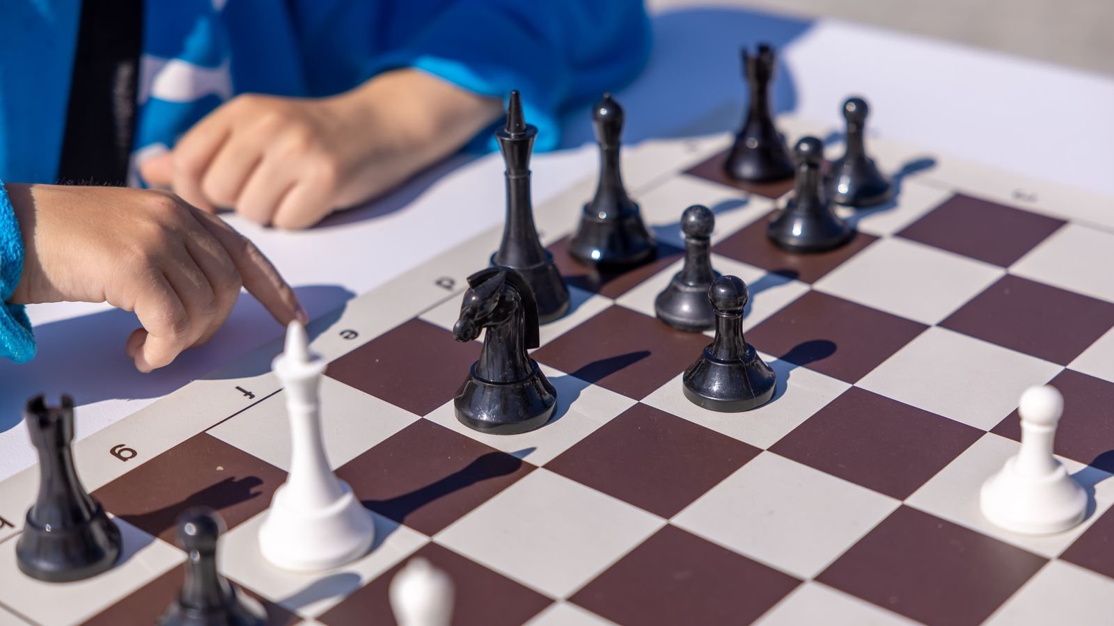 Close up of a child's hands moving a knight on a wooden chessboard during a live online chess lesson