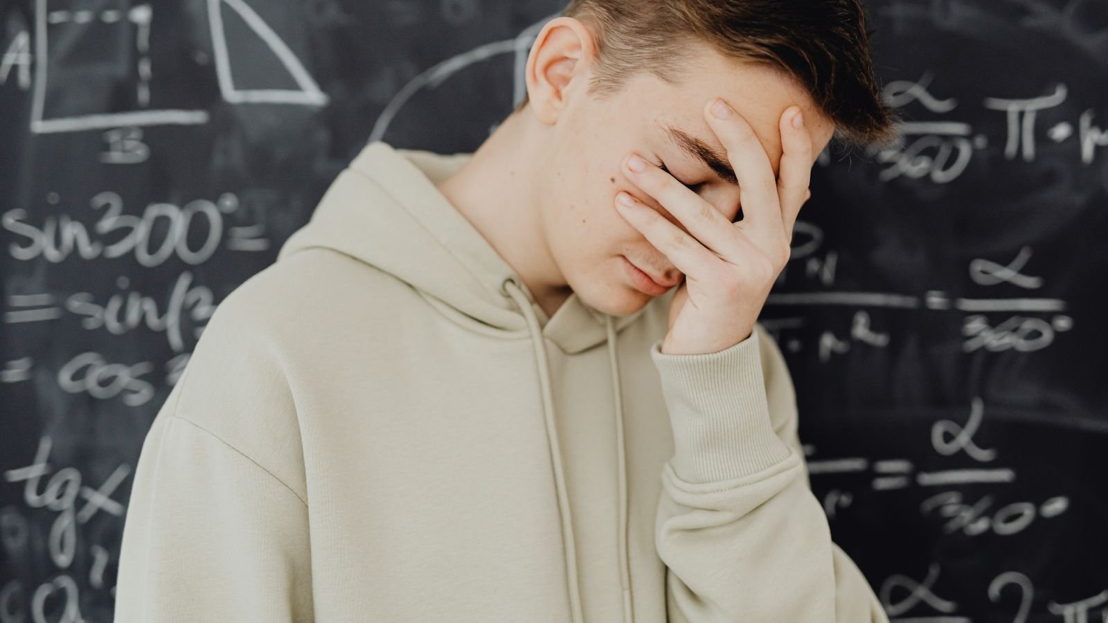 Child looking frustrated at a maths worksheet at home while a parent sits nearby